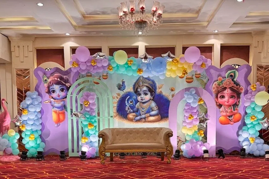 Birthday stage inside the hall with a pastel balloon garland, silver star balloons and a gold settee under the chandelier.