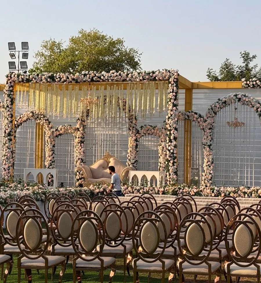 The floral wedding stage in daylight with rows of gold oval-back chairs set out on the lawn in front of it.