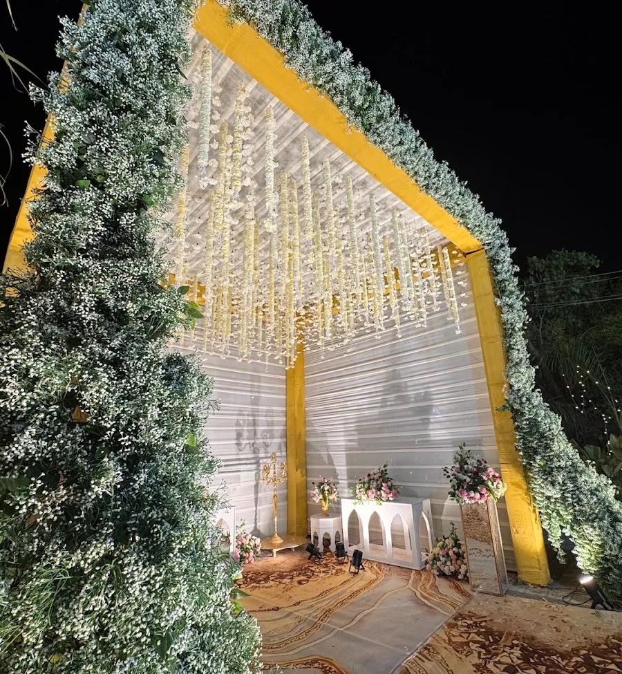 Tall arched pavilion built from white gypsophila and foliage on a gold-wrapped frame, with strands of white flowers hanging from its ceiling over an arched console table.