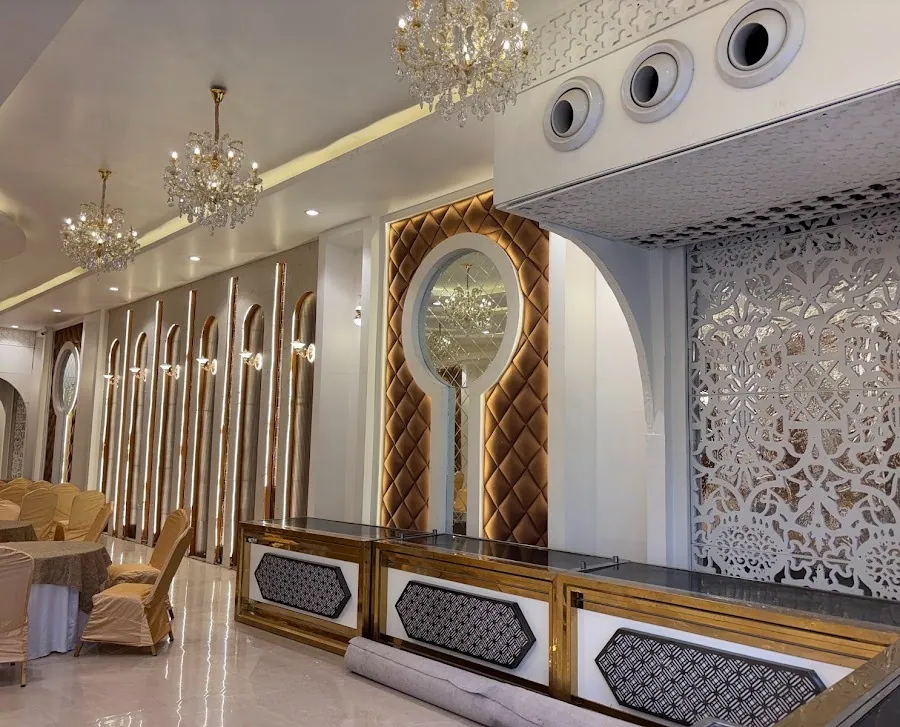Banquet hall detail: gold quilted feature wall with an oval mirror, arched mirror panels, a white jaali screen and the hall's gold-framed buffet counters on polished marble.