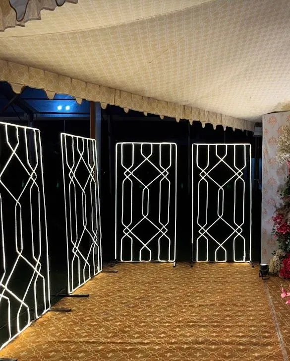 Night passage lined with tall glowing white jaali lattice light screens leading toward a floral wall.