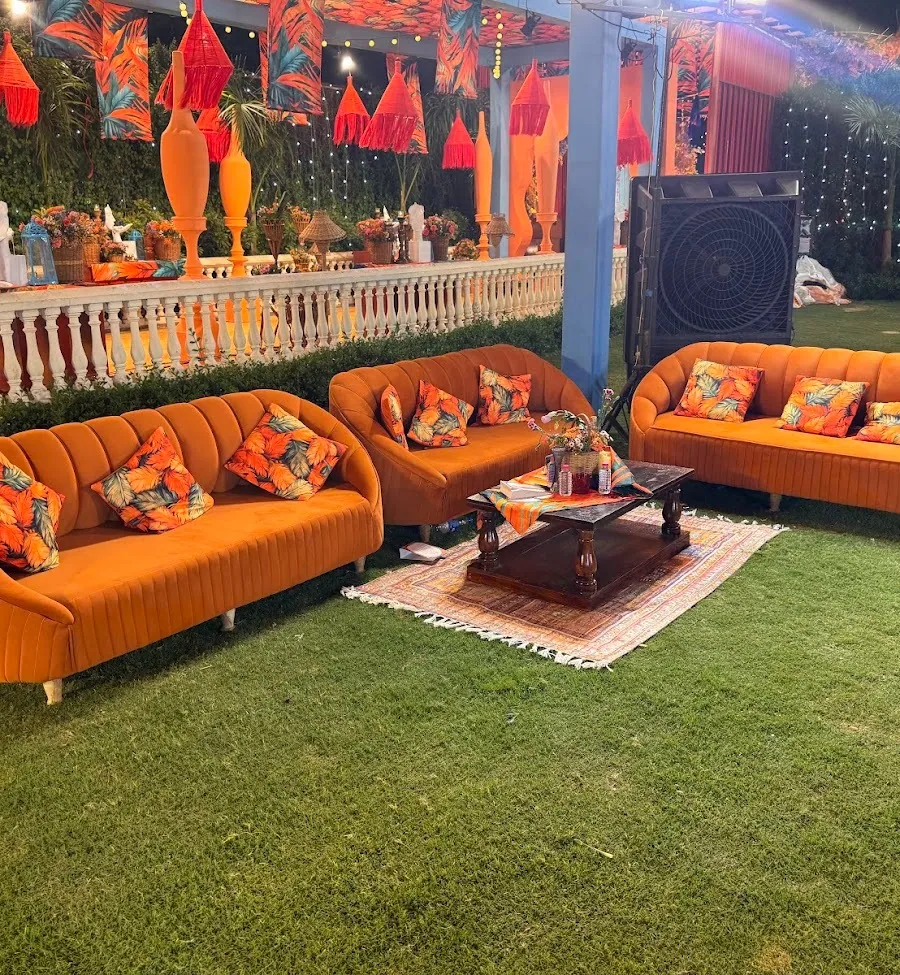 Night lounge on the lawn: burnt-orange tufted sofas with tropical print cushions around a wood table, string lights and red tasseled lanterns overhead.