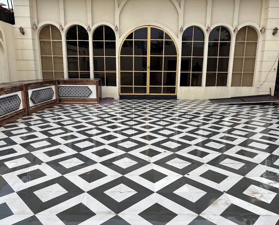 Black and white diamond-patterned marble courtyard in front of Madhavam's cream facade, with a row of arched windows and a gold-framed arched double door.