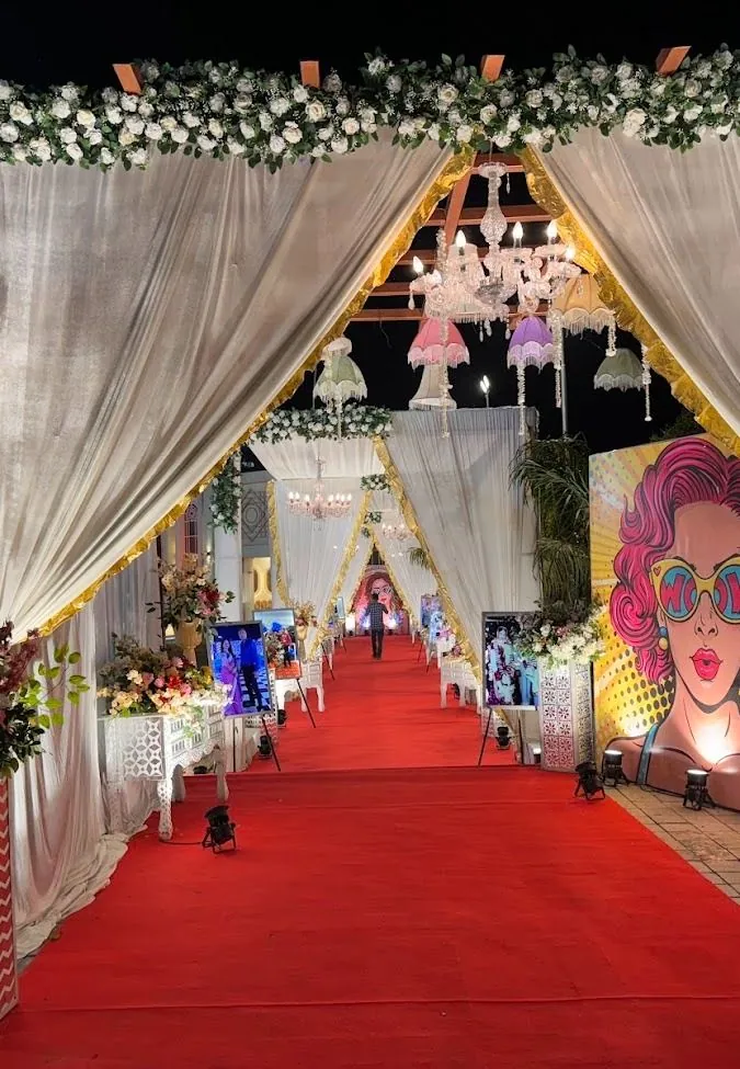 Red carpet running through a night-time corridor of peaked white and gold draped canopies hung with a crystal chandelier and pastel fringed lampshades.
